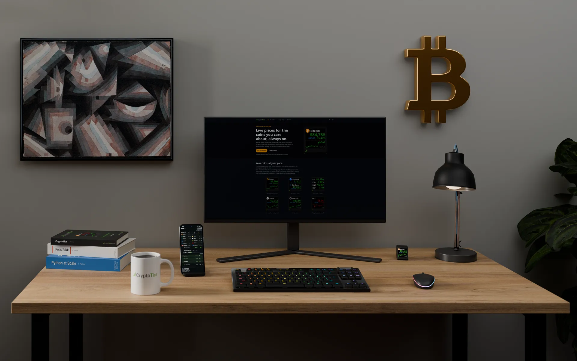 A CryptoTicr on a wooden desk beside a monitor, a phone on a stand, a coffee mug, a keyboard and a desk lamp